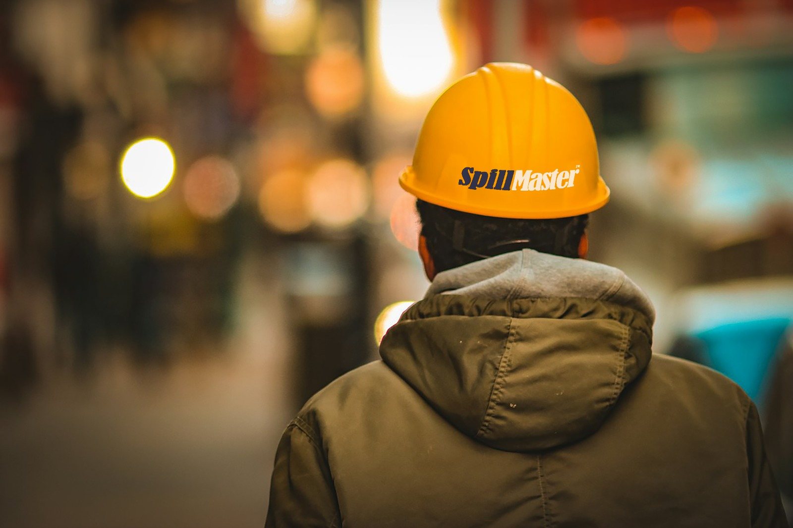 Industrial worker wearing a yellow SpillMaster™ hard hat on a busy site at dusk