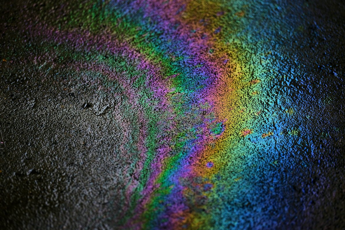Rainbow oil sheen spread across a dark concrete floor